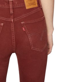 Jeans de mezclilla rojos con cintura alta, con un parche de cuero en la parte trasera y costuras características de Levi's en los bolsillos.