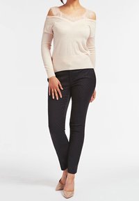 Light pink off-shoulder knit sweater with lace detailing and long sleeves, paired with black polka dot patterned slim-fit pants and nude heels.