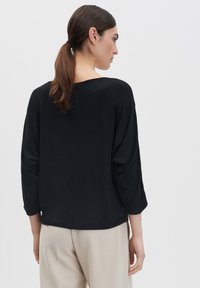 Top nero, ampio, con maniche a tre quarti, tessuto morbido e scollo ampio. Abbinate a pantaloni chiari.