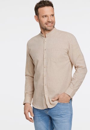 Camisa beige de botonadura con cuello mandarín, tela texturizada, un bolsillo en el pecho y dobladillo redondeado, combinada con jeans de color azul claro.