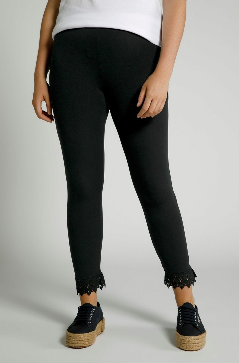 Zwarte leggings met een aansluitend ontwerp en kantafwerking bij de enkels. Het materiaal is soepel en rekbaar, gecombineerd met platform schoenen met veters.