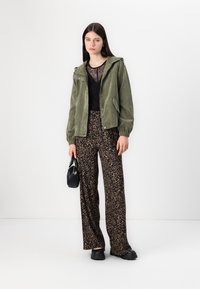 Oliven grønn cordfløyelsjakke med hette, svart blondebluse, leopardmønstret vide bukser og en liten svart håndveske.