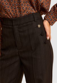 Czarne spodnie w cienkie prążki o gładkiej fakturze, z ozdobnym guzikiem i dwoma krytymi guzikami w pasie, zestawione z wzorzystym topem.