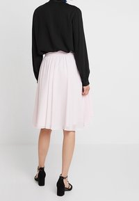 Blusa negra de manga larga combinada con una falda fluida de longitud hasta la rodilla en color rosa claro. La modelo lleva sandalias negras de tacón. Tela suave, diseño simple.