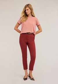 Svetle růžové tričko s kulatým výstřihem, přiléhavé vínové kalhoty s páskem a lesklé černé lodičky. Hladká látka; ležérní, elegantní styl; délka ke kotníkům.