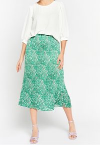 Vit blus med puffärmar, matchad med en grön, mönstrad midikjol. Kjolen har en flödig textur och en asymmetrisk nederkant.