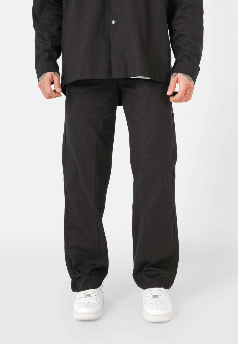 Pantaloni neri con un design a gamba dritta, dotati di tasche laterali e dettagli di cucitura delicati, abbinati a sneakers bianche.