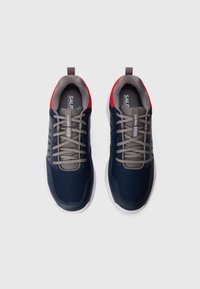 Baskets navy avec texture rayée, lacets gris et un accent rouge au talon. Elles comportent un col rembourré et une semelle en caoutchouc blanche.