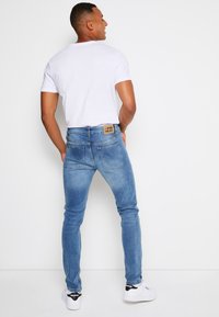 Slim-fit svetlomodré denimové džínsy s vyblednutou textúrou, dizajnom s piatimi vreckami a viditeľnou značkovou nálepkou na zadnom páse.