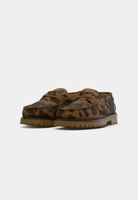 Sapatos de barco em pele com padrão de leopardo castanho e preto, com atacadores castanhos e solas de borracha texturizadas, sobre um fundo branco.