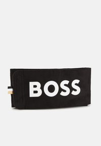 Musta kangast kott, millel on suur valge "BOSS" tekst, millel on kuldne aksent ja triibuline detail küljel. Sujuv tekstuur, ristküliku kuju.