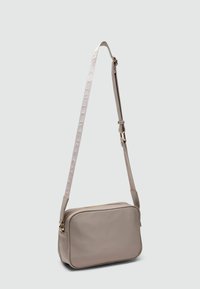 Geom bag de umplere sintetic de culoare bej, cu forma dreptunghiulara, inchidere cu fermoar si o curea texturata cu detalii de branding.