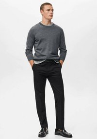 Suéter de punto gris sobre una camisa gris claro, combinado con pantalones negros y zapatos de cuero negros. Ajuste slim, diseño casual.