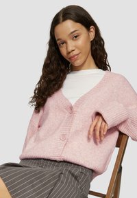 Helles rosa gestricktes Cardigan mit V-Ausschnitt, gerippten Bündchen und zwei Knöpfen vorne. Kombiniert mit einem gestreiften grauen Rock.