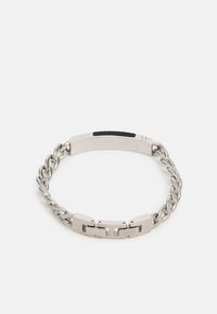 Bracelet en métal argenté avec un design de chaîne torsadée, des maillons plats et un accent central noir mat. La fermeture est lisse et intégrée.