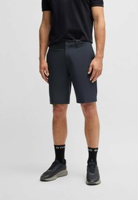 Herren Shorts in Dunkelgrau aus einem glatten, leichten Material. Mit einem Knopfverschluss und Seitentaschen, kombiniert mit schwarzen Sneakers und Socken.