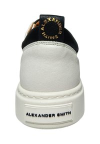 Sneaker bianca in pelle con un pannello per il tallone nero, caratterizzata da un logo dorato sulla linguetta del tallone e una suola testurizzata per una presa migliorata.