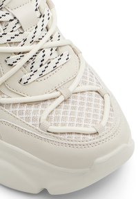 Baskets beiges avec une tige en maille texturée et des détails en cuir lisse. Présentent des lacets croisés et une semelle épaisse et texturée.