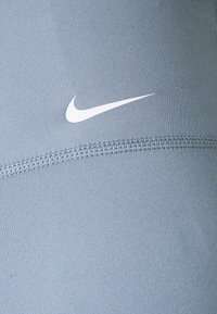 Světle modrá sportovní textilie s hladkou strukturou, na níž je bílý logo Nike. Podél okraje jsou viditelné švy.
