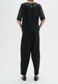 Top nero con perline, maniche corte e dettaglio a chiave sul retro, abbinato a pantaloni neri larghi e scarpe basse. Aspetto testurizzato e a strati.