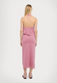 Abito midi senza spalline e senza schiena, a righe rosa e bianche, realizzato in tessuto morbido con una silhouette fluida, caratterizzato da un fiocco nella parte posteriore del collo.