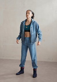 Világoskék sportos tréningruha cipzáros dzsekivel és beszűkített nadrággal. Sötétzöld crop top fölött viselve; fekete és piros magasszárú cipők.