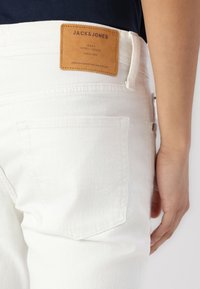 White jeans made from denim, featuring a brown leather patch labeled "JACK & JONES" with stitching accents and a back pocket design.