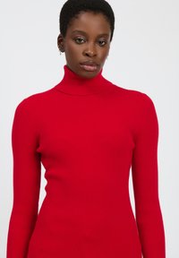 Maglione a collo alto rosso a coste con maniche lunghe e una forma aderente. La texture è liscia con dettagli a coste verticali.
