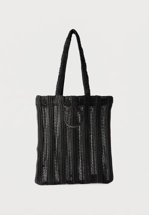 Black knitted tote bag with vertical open weave stripes and two handles, featuring a circular decorative buckle on the front.