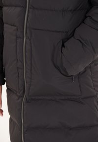 Sort pufferjakke med lynlås. Har en glat overflade, to forlommer og et quiltet design for isolering.