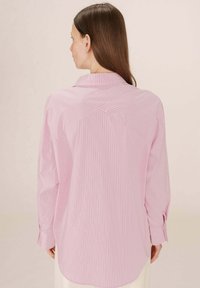 Camicia a maniche lunghe a righe rosa con spalla posteriore, dotata di colletto volante e polsini regolabili, realizzata in tessuto leggero.