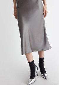 Abito midi grigio seta con una forma fluida, abbinato a calzini neri a coste e tacchi alti argentati lucidi con punta affusolata e tacchi sottili.