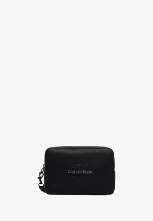 Pochette rettangolare nera Calvin Klein con logo CK inciso e tracolla laterale staccabile su sfondo bianco semplice.