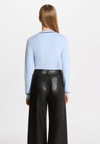 Maglietta a maniche lunghe a coste di colore azzurro chiaro abbinata a pantaloni wide-leg in pelle nera a vita alta. Sottile cucitura nera sulle tasche posteriori dei pantaloni.