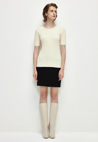 Top corto de punto acanalado blanco de manga corta combinado con una falda negra y botas beige hasta la rodilla, mostrando una silueta ajustada y texturas suaves.