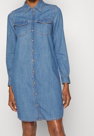 Robe-chemise en jean à manches longues avec boutons à l'avant, deux poches poitrine à rabat et un col, portée par une personne de la nuque au milieu des cuisses.