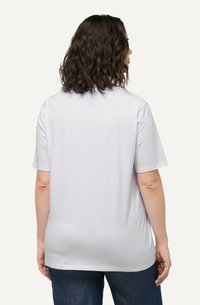 Camiseta blanca de manga corta fabricada en algodón, con un corte holgado y un escote redondo, vista desde atrás, combinada con jeans azules.
