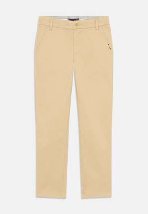 Pantalon beige slim fit avec poches avant, passants pour ceinture, fermeture par boutons et petit détail drapeau près de la poche droite.