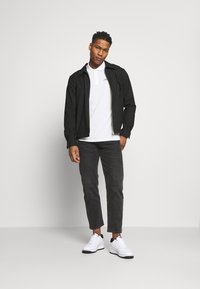 Black striped jacket over a white polo, gray jeans, and white sneakers. Contrasting patterns with a zip closure on the jacket.