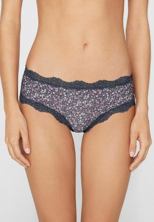 Woman wearing dark floral patterned hipster panties with lace trim, shown from waist to mid-thigh against neutral background.