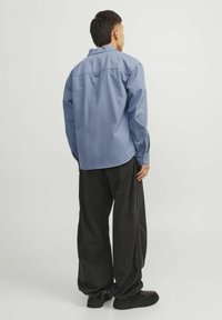 Chemise à manches longues bleu clair avec un ourlet arrondi et des poignets à boutons, associée à un pantalon noir ample et des chaussures noires. Design minimaliste.