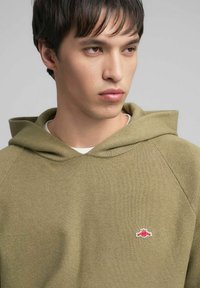 Felpa con cappuccio verde oliva con trama a coste, caratterizzata da un piccolo logo rosso sul petto e un cappuccio dal taglio morbido.