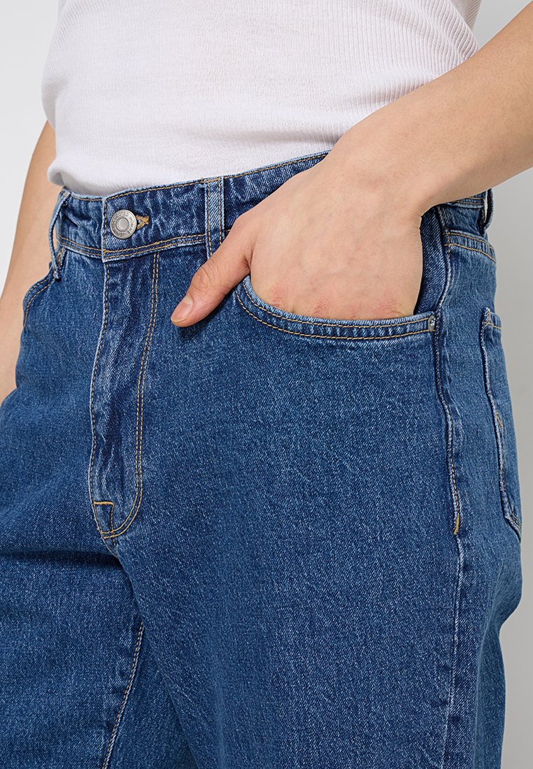 High-waisted denim jeans in medium blue met een klassieke pasvorm. Kenmerken zijn onder andere voorzakken, koperen stiksels en een metalen knoopsluiting.