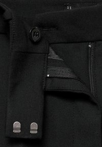 Pantaloni neri con tasca con zip, chiusura con bottone e accessori in metallo argentato. Il tessuto è strutturato e presenta una finitura liscia.