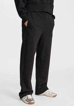 Svarta sweatpants med en avslappnad passform, sidfickor och en slät textur, kombinerade med silverfärgade sneakers och en vit sula.