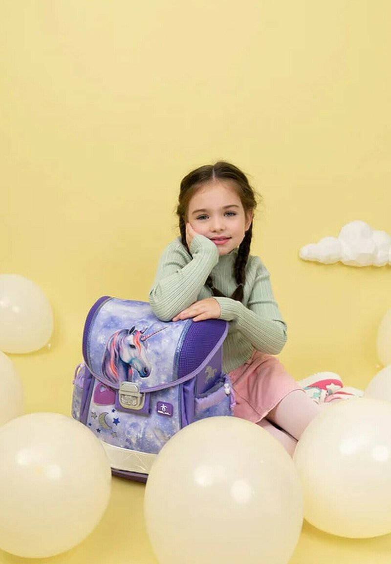 Lila Rucksack mit Einhorn-Design, strukturierten Oberflächen, mehreren Fächern und grauen Beschlägen, vor einem gelben Hintergrund mit Ballons.
