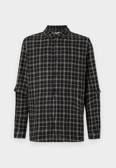 Melnā krekls ar kvadrātveida rakstu bēšā krāsā. Pogājams priekšpuse, klasiskā apmale, garas piedurknes ar brīvu piegriezumu un sānu šķēlumiem.