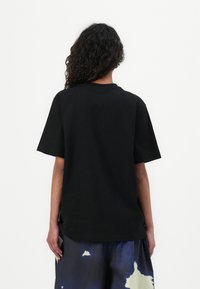 Camiseta de algodón negra con mangas cortas y escote redondo, que presenta un corte holgado y un diseño minimalista.