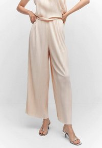 Bleke perzikkleurige wijde broek met verticale plooien en een elastische tailleband, gecombineerd met zilveren gekruiste hakken. Soepele, lichte stof.