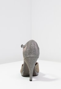 Scarpa con tacco alto in tessuto metallico argento con finitura testurizzata, punta affusolata e un dettaglio a fiocco sul tallone.